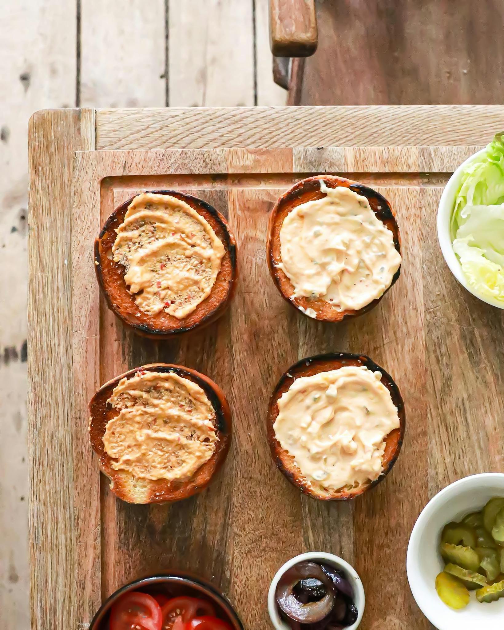 Top-down view of burger preparation with fresh ingredients on a wooden surface.